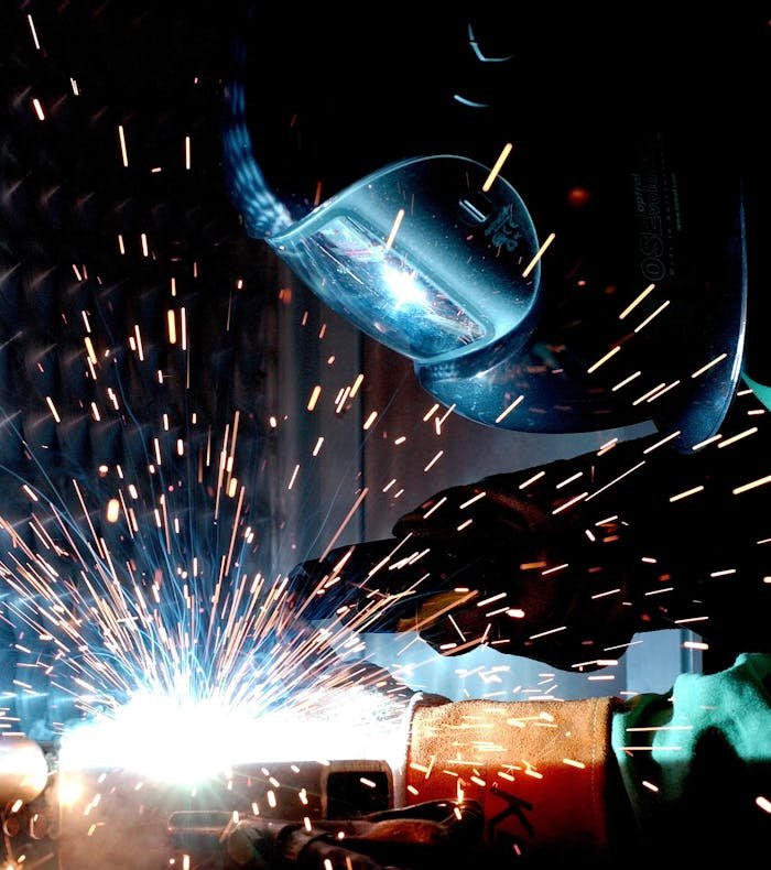 Albañilería en Madrid. A focused welder works with metal in an industrial setting, creating vibrant sparks.